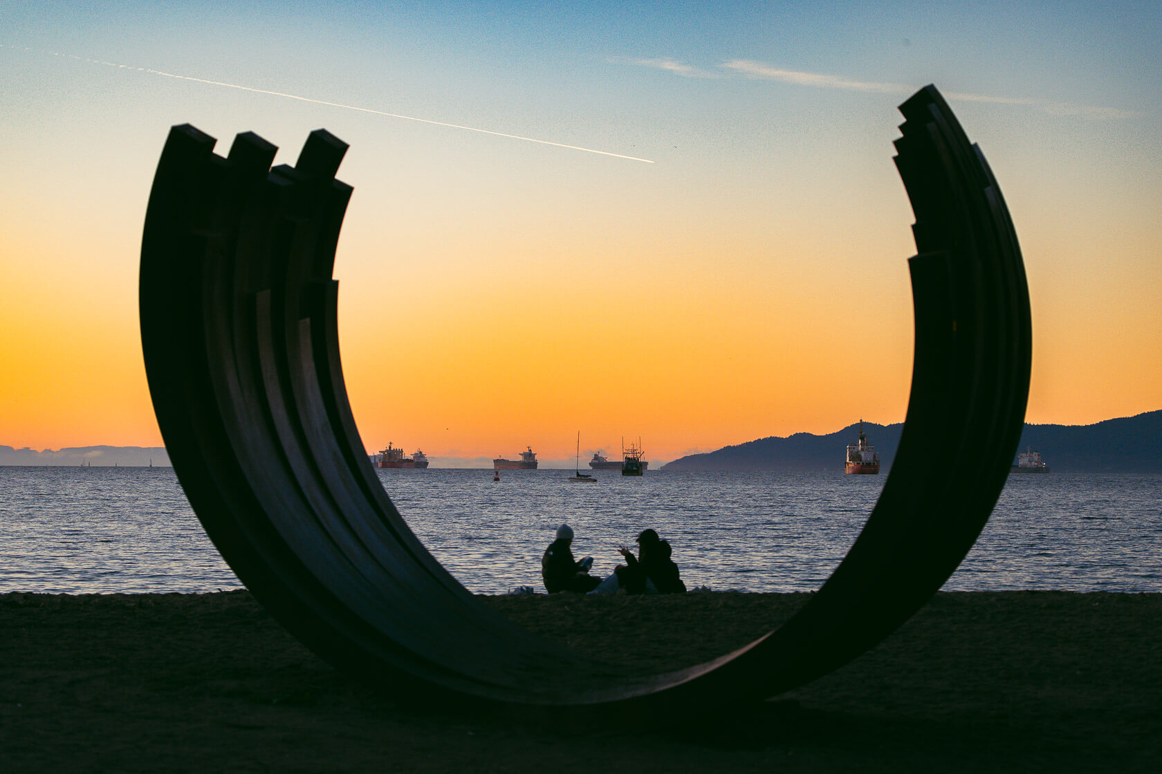 Couple framed by the Arc Sculpture on Sunset Beach